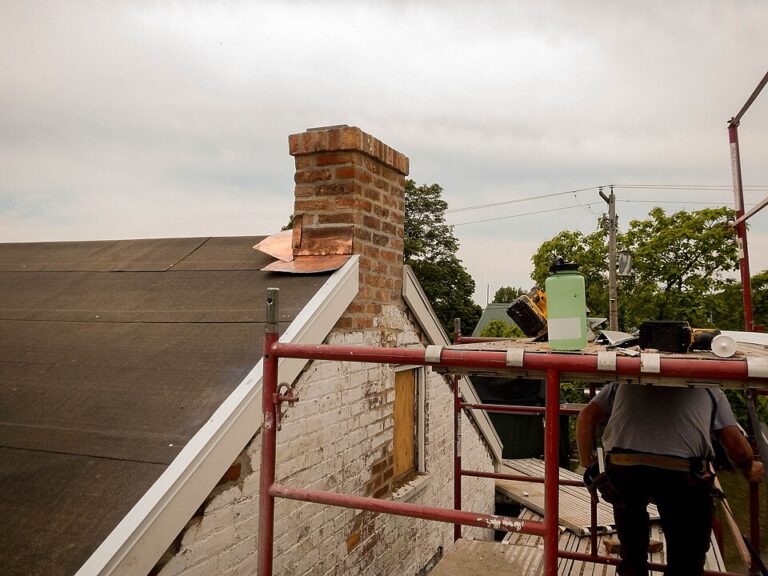 Conservation tradesperson installing copper flashing beside a brick chimney