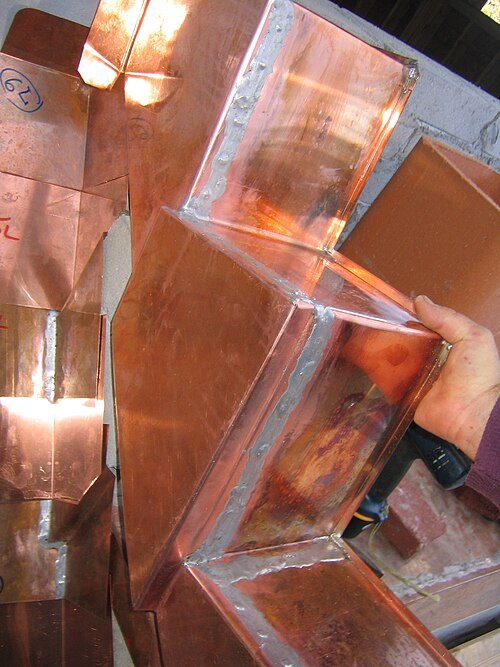 Copper step flashing and counterflashing fitted around a masonry chimney